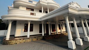 A multi-story building with a white facade, columns, and a paved entrance area. - Spacious, fully air-conditioned 4-bedroom ensuite home (Perumbavoor)