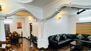 A spacious living area with a marble floor, a black leather sofa, a dining set, and a staircase with ornate railings. - Spacious, fully air-conditioned 4-bedroom ensuite home (Perumbavoor)