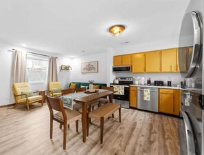 A modern kitchen with yellow cabinets, a dining area with wooden furniture, and a large refrigerator. - Branson Family Haven (New Deck) First Responder (Branson)