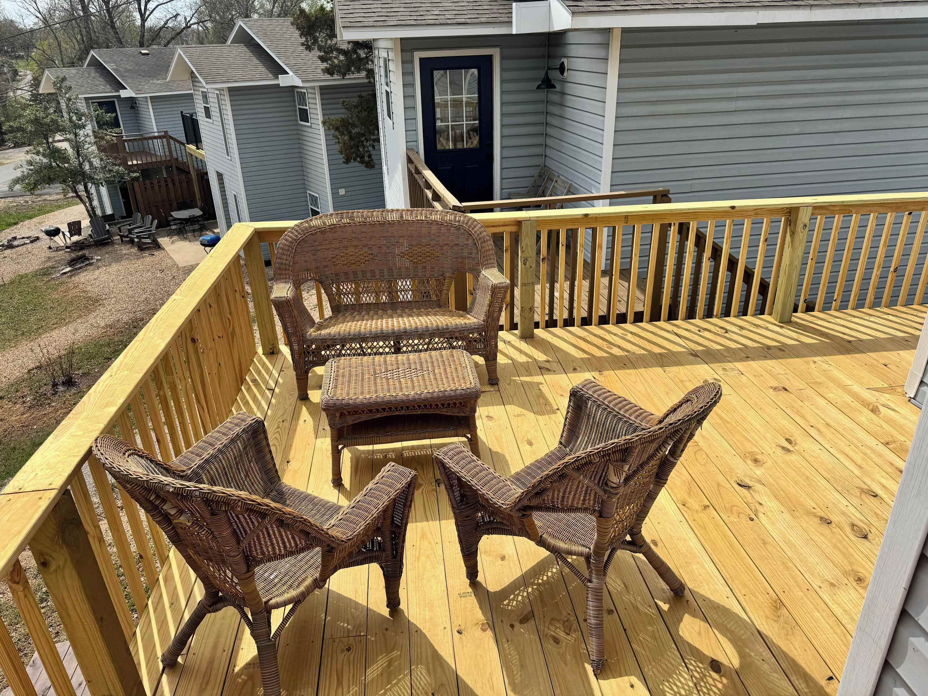 A wooden deck with wicker furniture, a railing, and a house in the background.