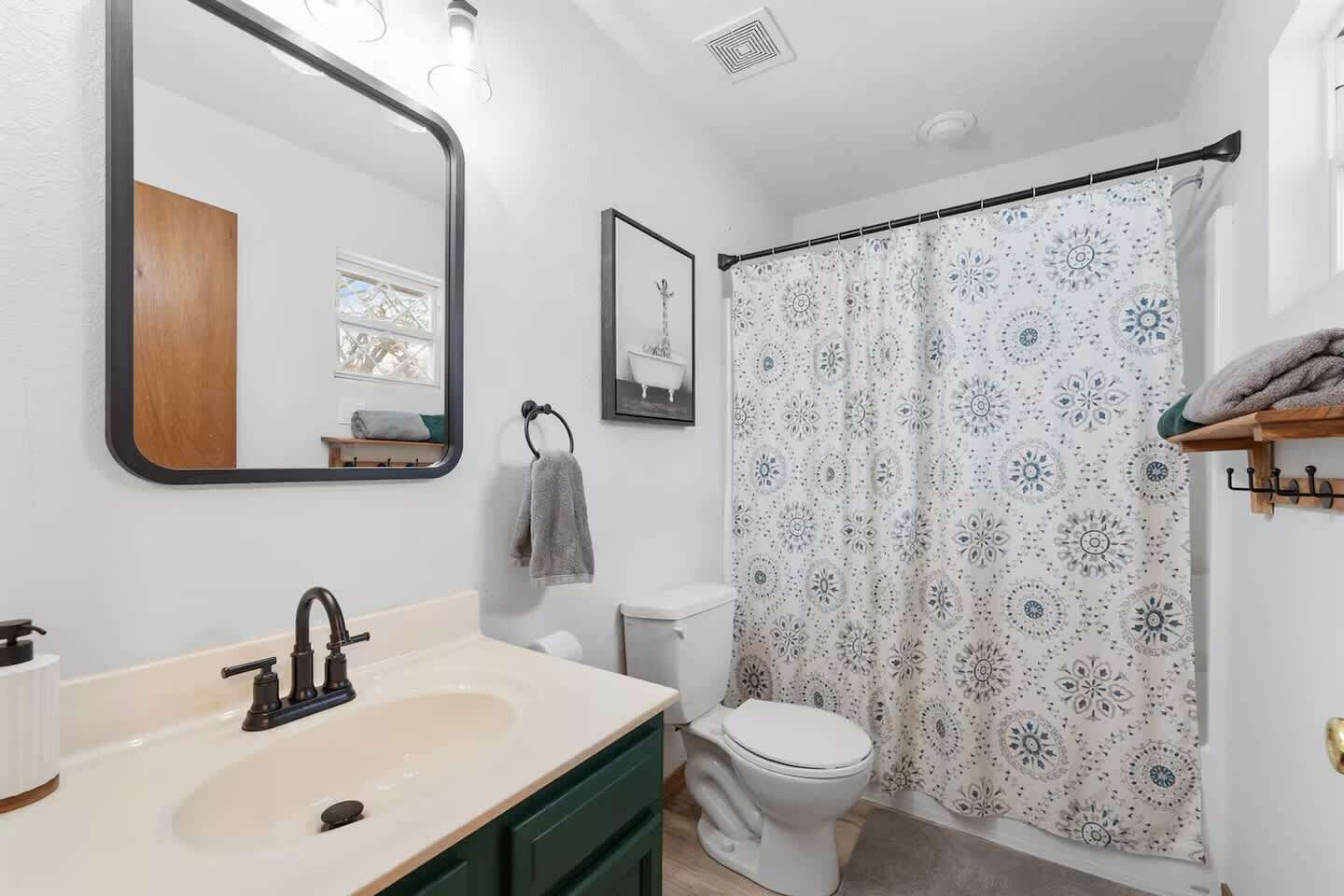A bathroom with a sink, mirror, toilet, and shower curtain.