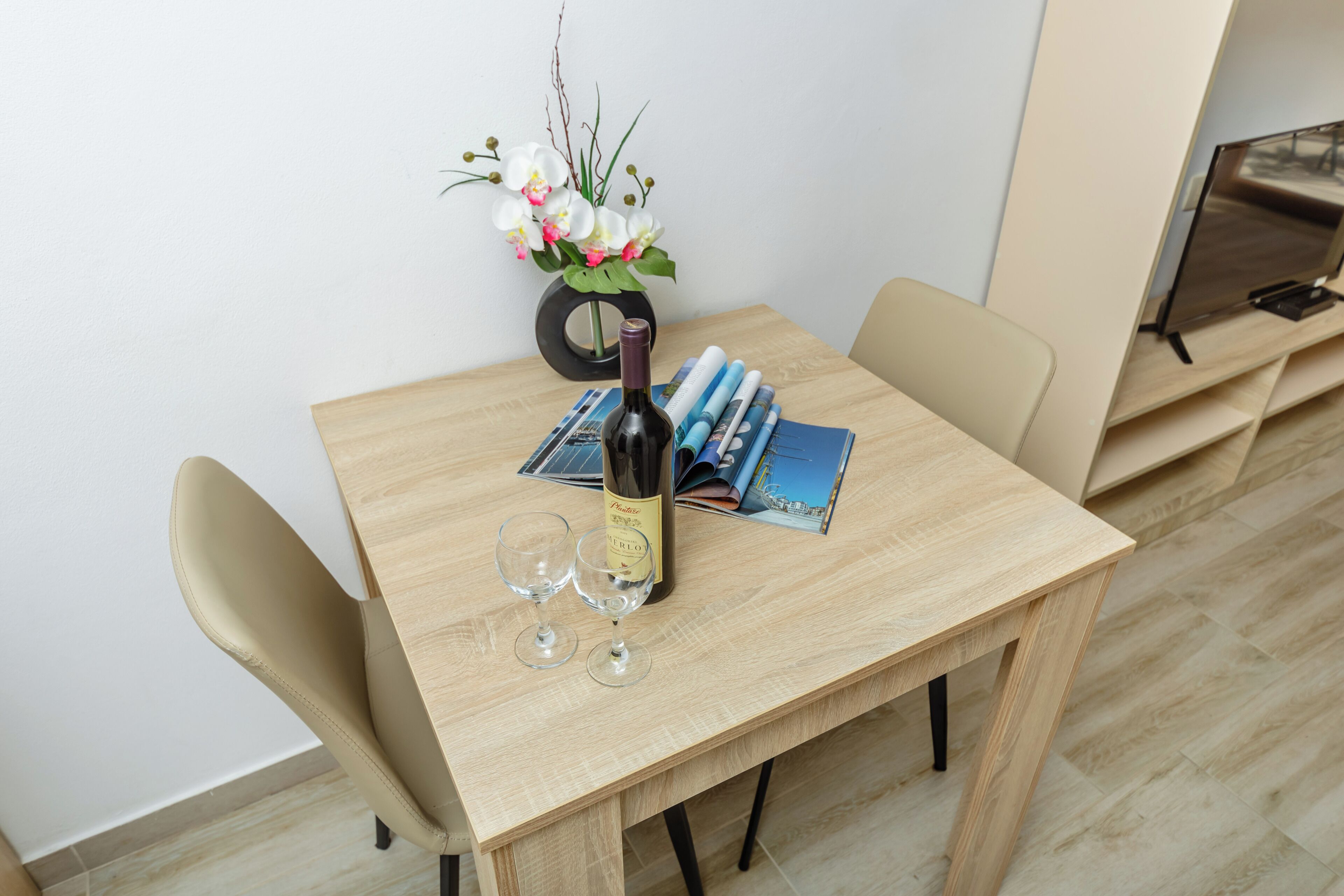A wooden table with a bottle of wine, two glasses, and a vase of flowers.