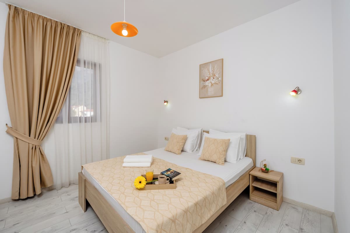 Un dormitorio ordenado con cama, mesita de noche y ventana con cortinas.