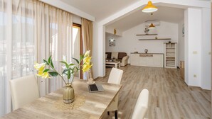 Amplia sala de estar con una mesa de comedor, sillas, una computadora portátil y un jarrón con flores.