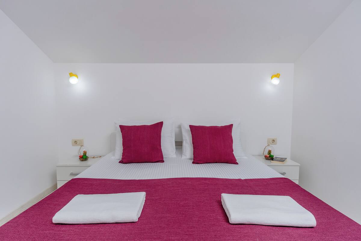 Una habitación de hotel con una cama, dos mesitas de noche y dos luces fijadas a la pared.