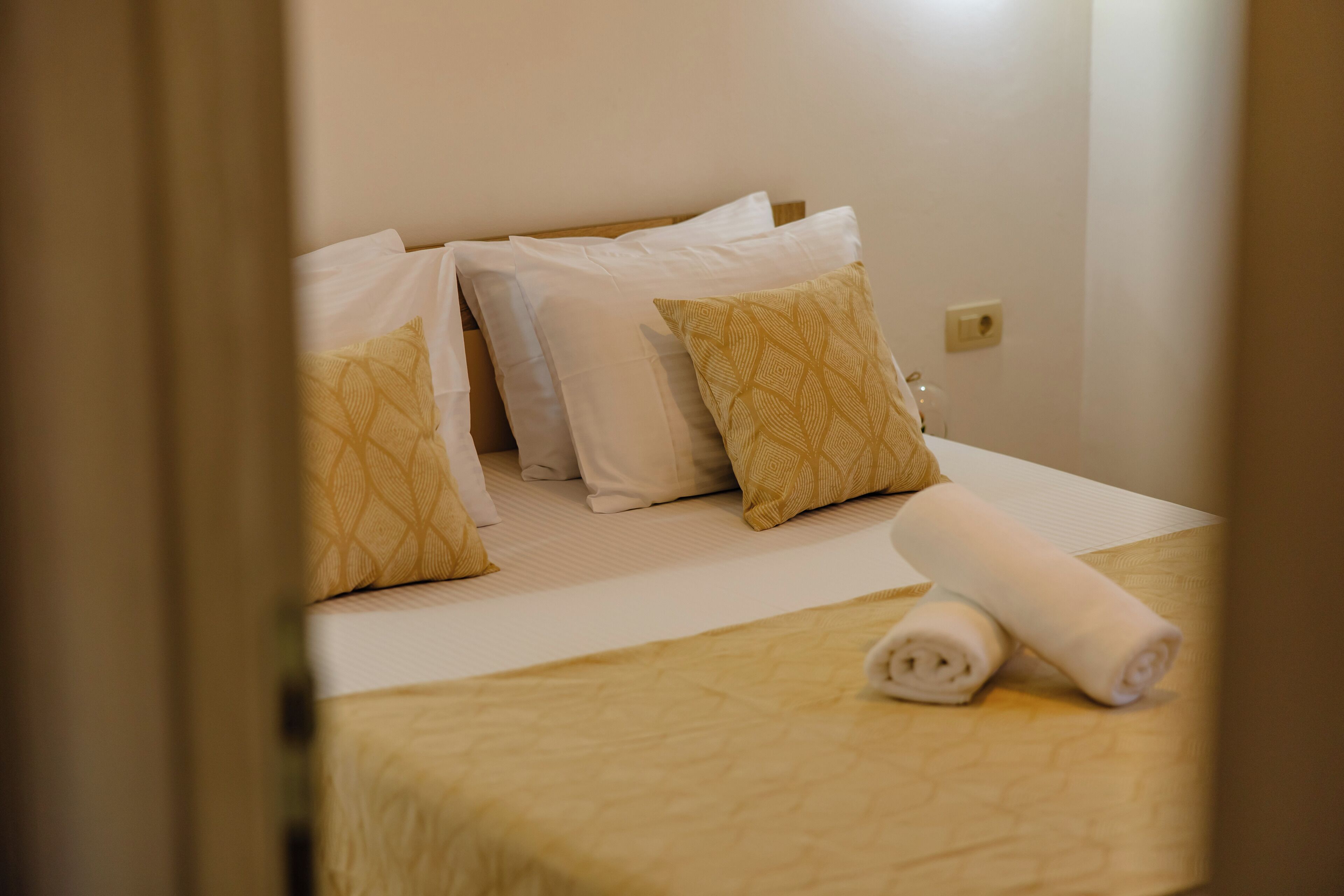 A hotel room with a bed, pillows, and a rolled towel.