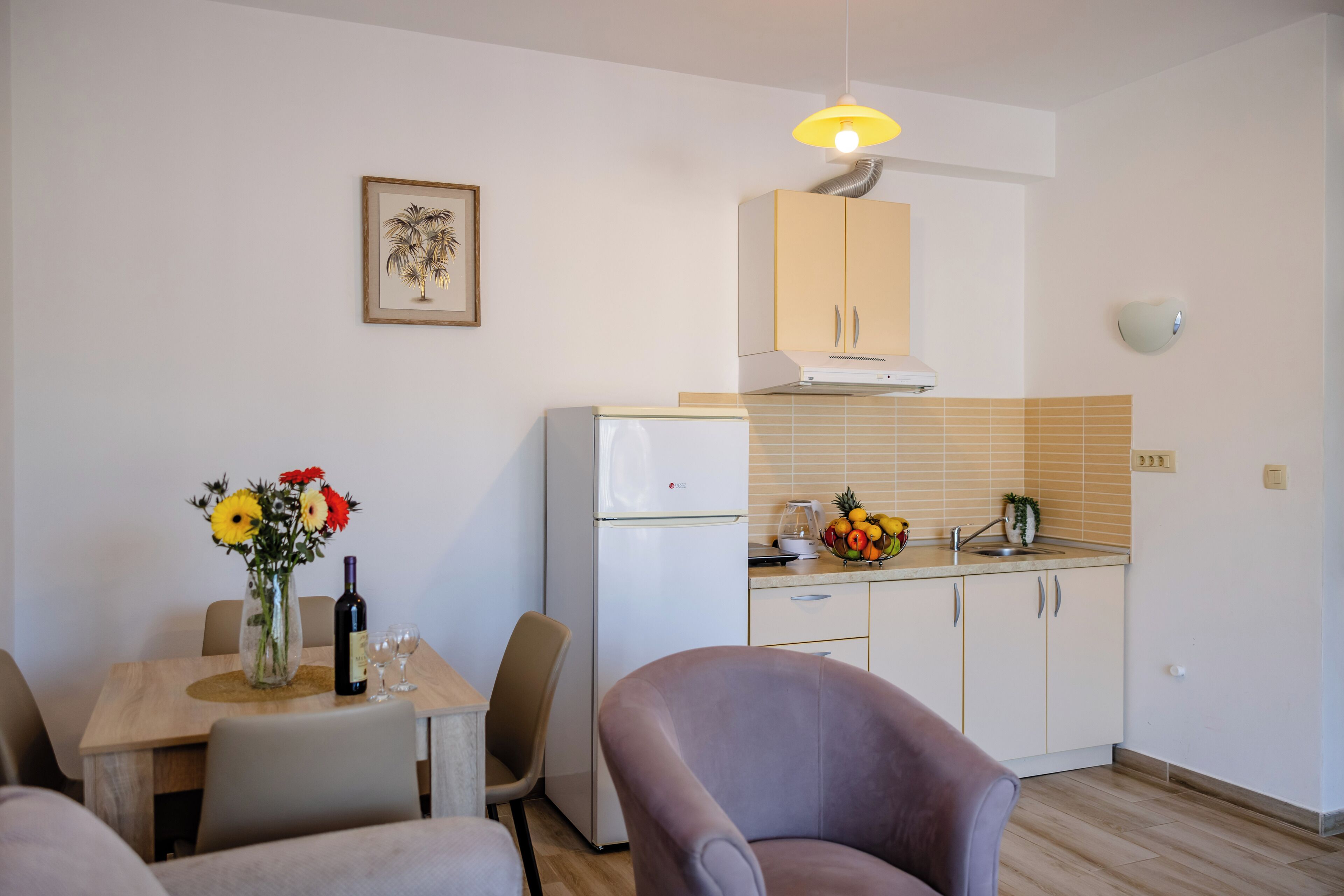 A compact kitchen with a refrigerator, a dining table with chairs, and a vase with flowers.