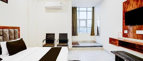 A hotel room with a bed, two chairs, a TV, a desk, and a window.