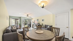 Ein Essbereich mit einem runden Holztisch und Stühlen, einer Couch mit Kissen, einem Deckenventilator und einer Tür.