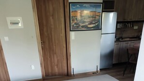 Een kamer met een bed, een houten deur, een keukenhoek en een lijst met een foto aan de muur.