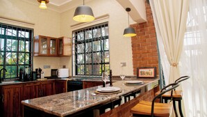A kitchen with wooden cabinets, a marble countertop, a microwave, and hanging pendant lights. - Cosey Farm House and tent near  Ngorongoro, Serengeti and Manyara destinations. (Karatu - Arusha)