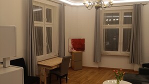 Olohuoneessa on puulattia, ruokapöytä, sohva, pieni valkoinen pöytä, jossa on kukkia, sekä kattovalaisin.