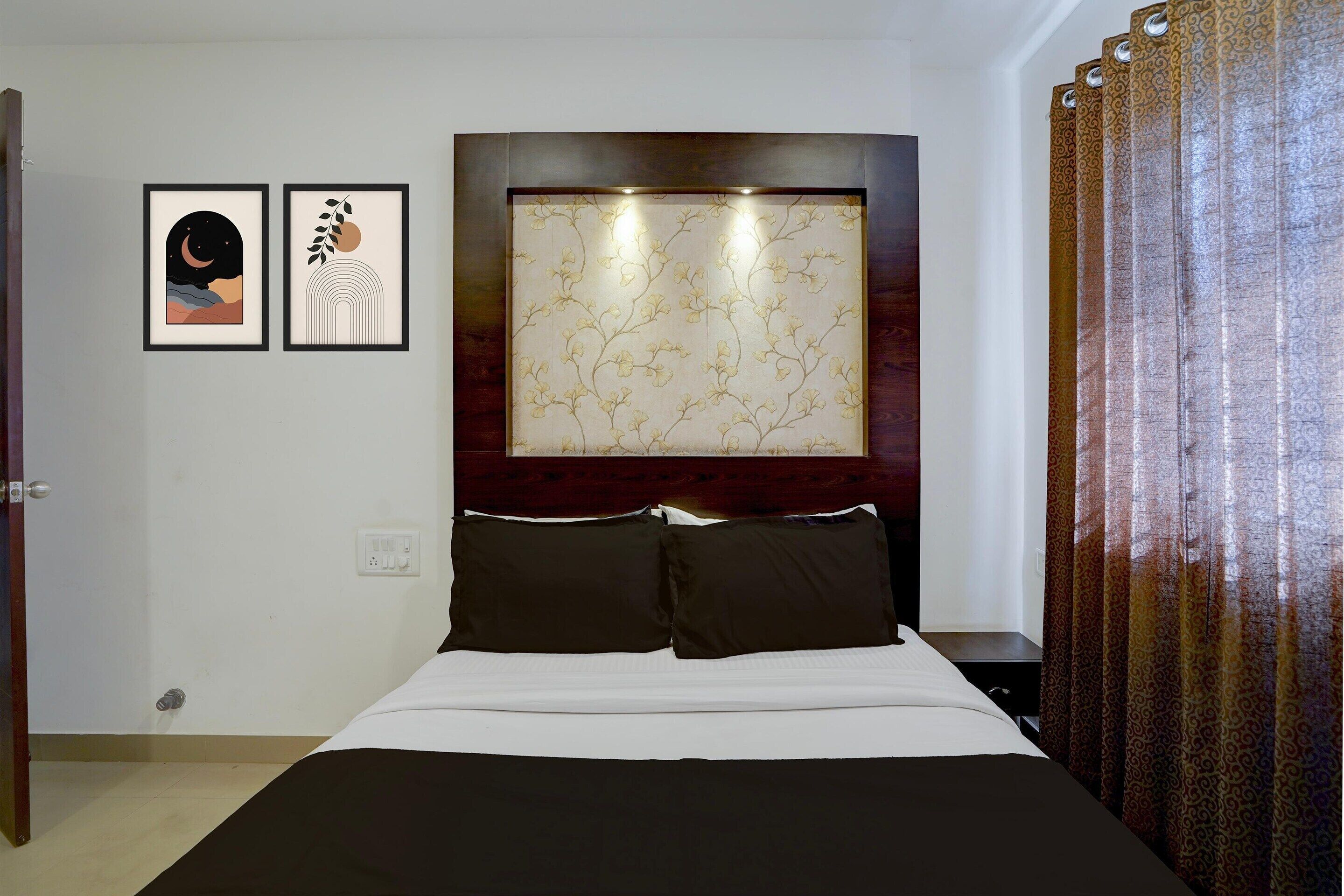 A hotel room with a bed, two framed artworks on the wall, a patterned headboard, and a curtain.