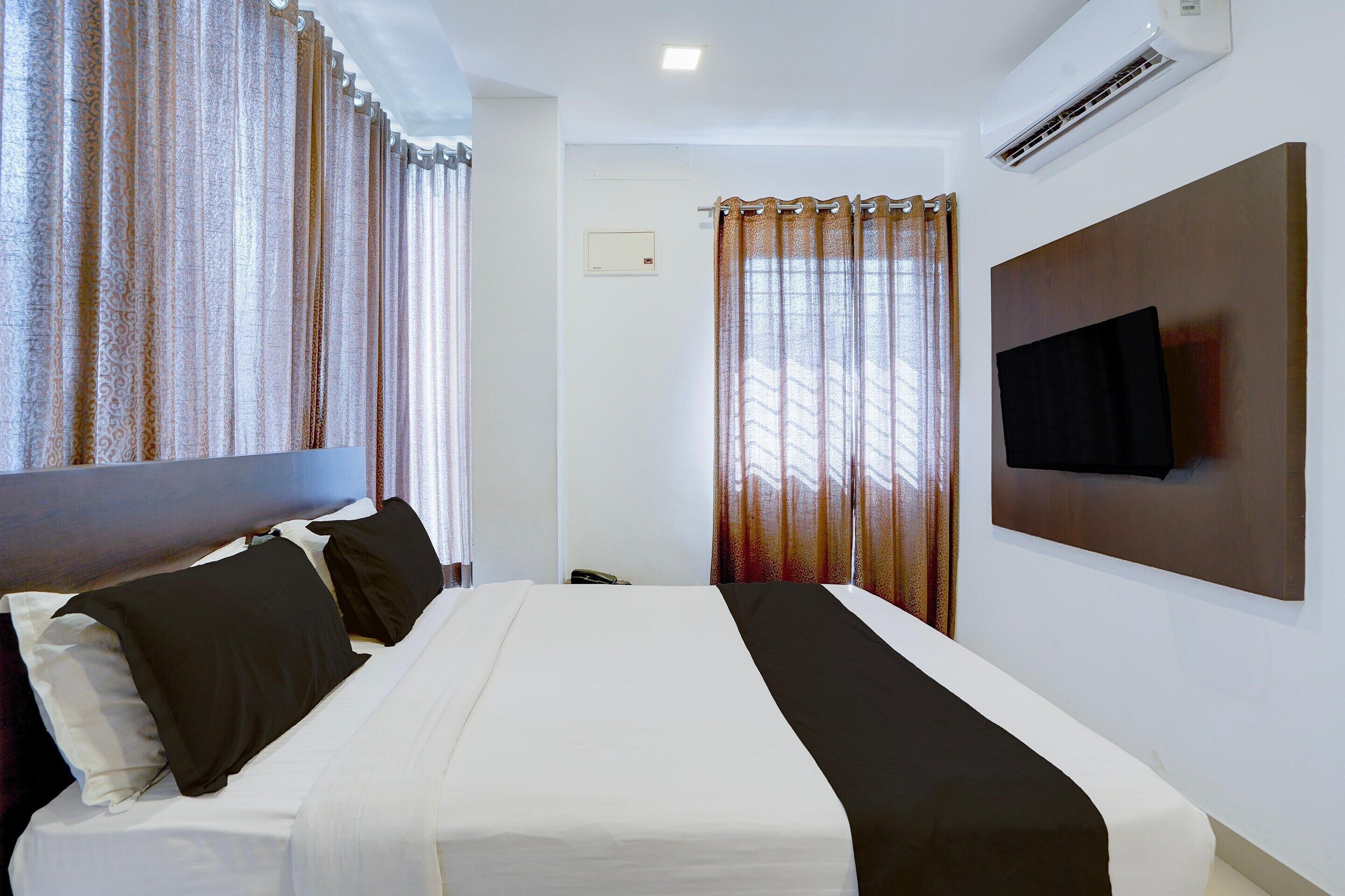 Une chambre d’hôtel équipée d’un lit, de rideaux, d’un téléviseur fixé au mur et d’un appareil de climatisation.