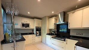 A modern kitchen with white cabinets, a black countertop, stainless steel appliances, and a glass wine rack. - Stylish Dulwich Apartment With Parking (London)
