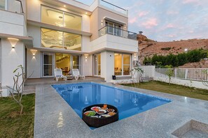 A modern two-story house with a swimming pool, outdoor seating, and a landscaped garden.