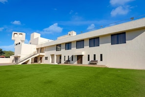 A modern building with a flat roof, a staircase leading to the entrance, and a well-maintained lawn.