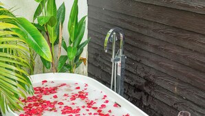 A bathtub filled with water and rose petals, a wooden tray with two glasses, and a potted plant beside it. - ELIVAAS Casa Del Mar 4BHK Villa & Pool (Anjuna)