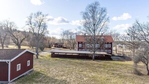 A red barn and a multi-story building with a red roof, surrounded by trees and open fields.