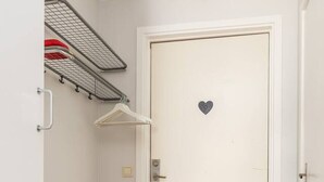A white door with a heart-shaped decoration, a black doormat, a radiator, and a metal shelf with clothes.