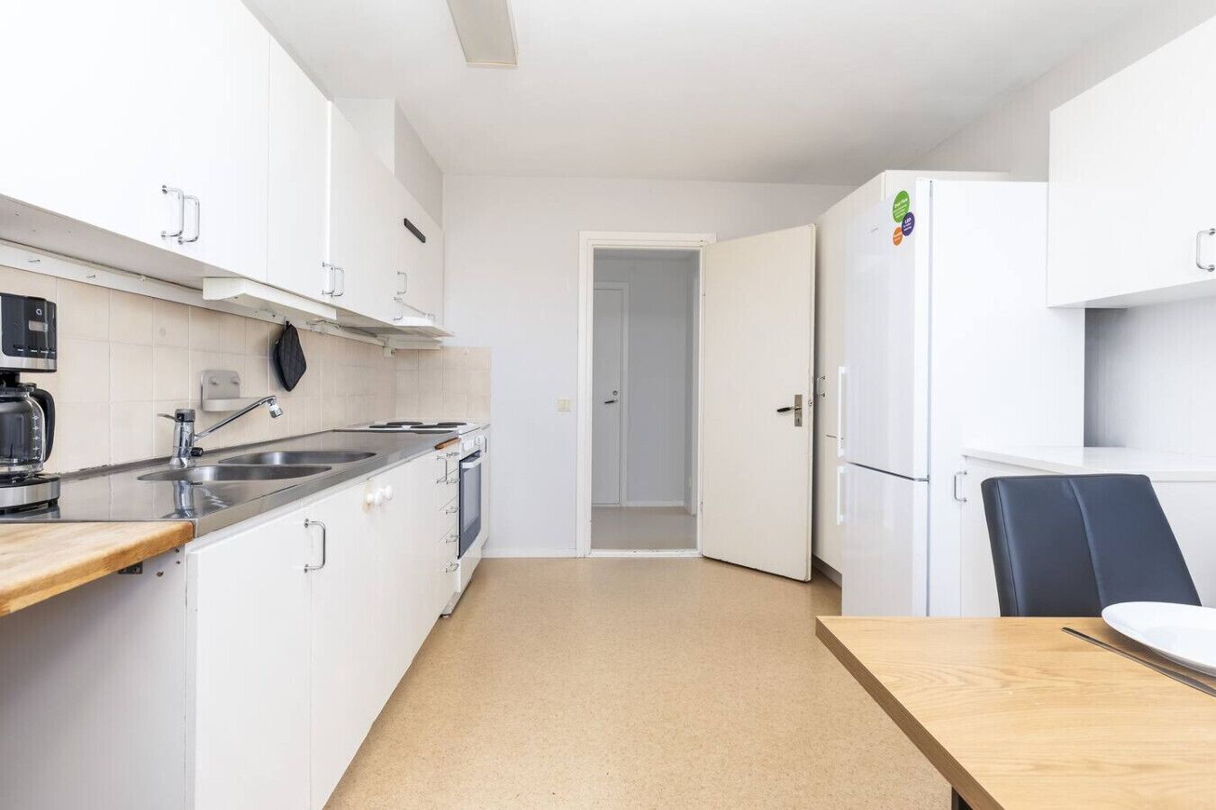 Cocina compacta con gabinetes blancos, estufa, lavabo y refrigerador.