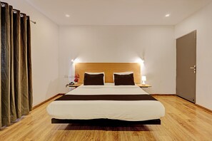 Een hotelkamer met een groot bed, een houten hoofdeinde, nachtkastjes met lampen en een deur.