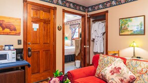 Une chambre d’hôtel avec une porte en bois, un lit, un canapé rouge, un tableau, une lampe et un four à micro-ondes posé sur le comptoir.