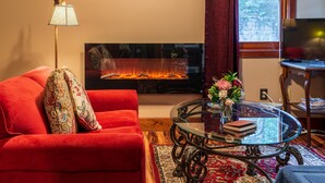 Een woonkamer met een rode bank, een glazen salontafel, een open haard en een televisie.