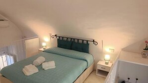 Un dormitorio con una cama, dos mesitas de noche con lámparas, una ventana y un objeto decorativo en la mesita de noche.