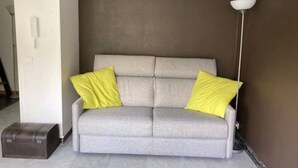 Un sofá gris con dos almohadas amarillas, una lámpara de pie y un objeto marrón pequeño sobre el suelo.