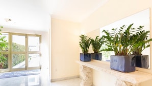 Un interior luminoso con piso de mármol, un banco blanco con plantas en macetas y un ventanal con vistas al verdor.