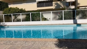 Una piscina con suelo de piedra, rodeada por una valla blanca y vegetación.