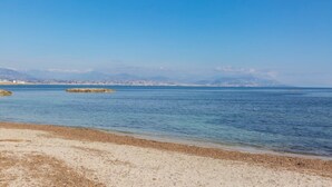 Una playa costera con agua cristalina, arena dorada y montañas a lo lejos.