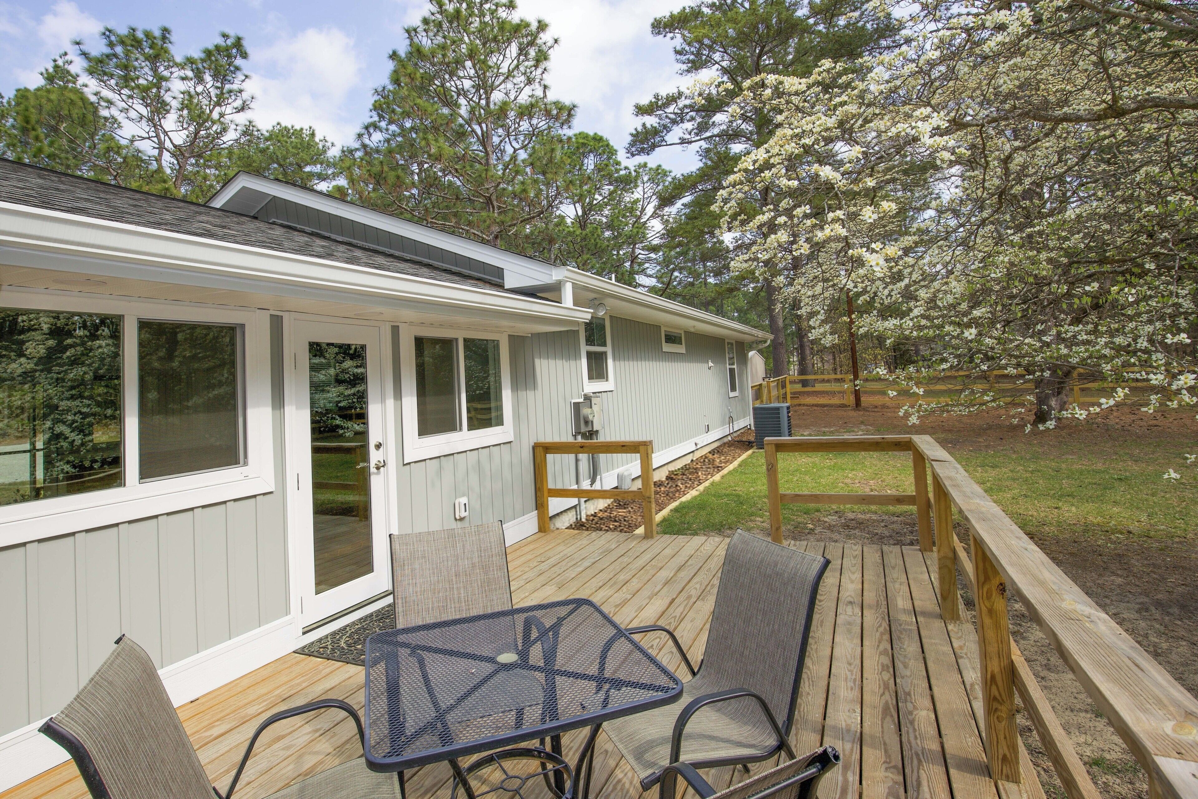 Une terrasse couverte avec une table et des chaises, une terrasse en bois et une maison avec de grandes fenêtres et une porte.