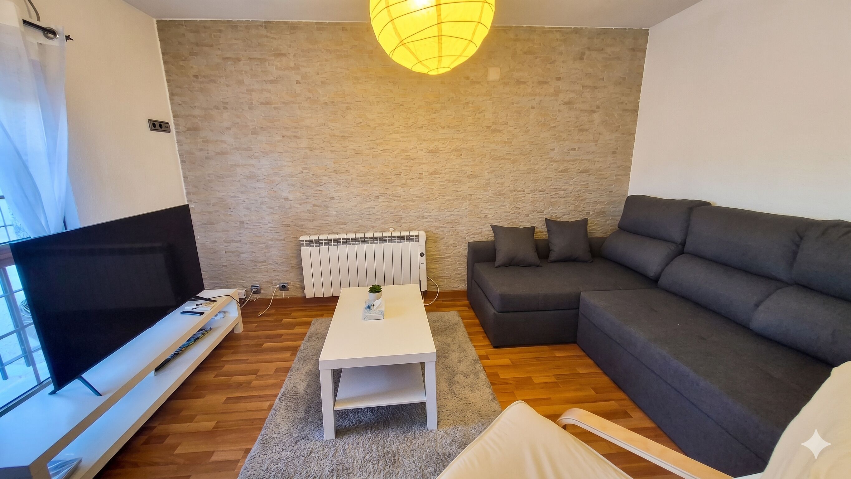 A living room with a TV, sofa, coffee table, and a radiator.