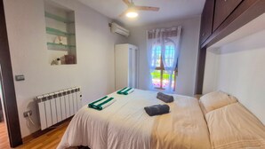Un dormitorio con una cama, un radiador, un ventilador de techo, una ventana con cortinas y un armario.