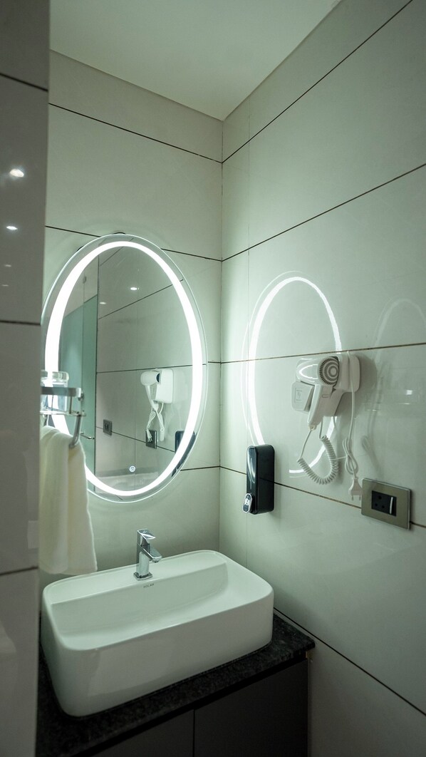 A modern bathroom with a large mirror, a sink, and a hairdryer mounted on the wall. - The Blues Hotel Golden Glory Rajkot (Rajkot)