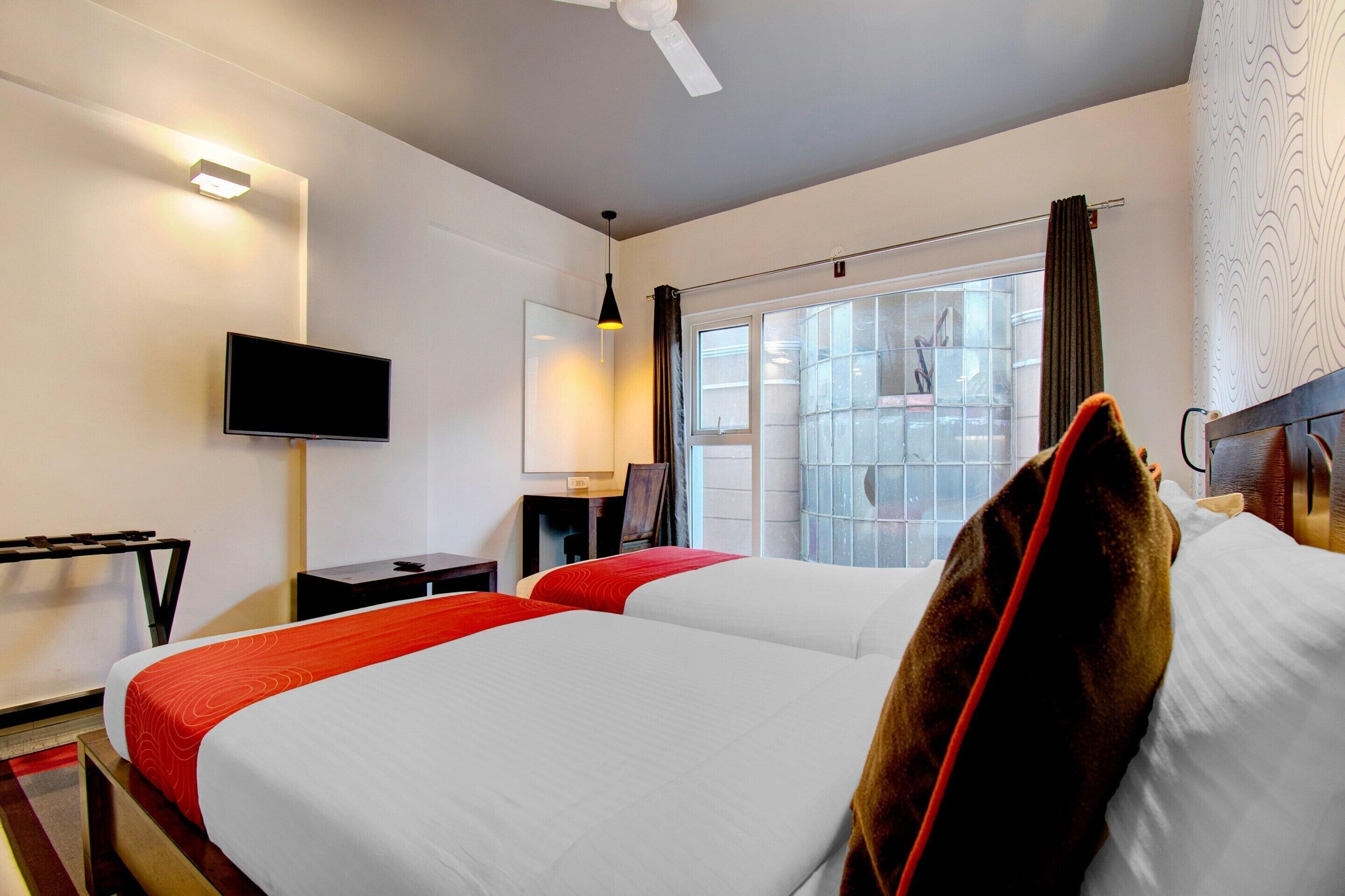 A hotel room with two beds, a flat-screen TV, a desk, and a window with curtains.