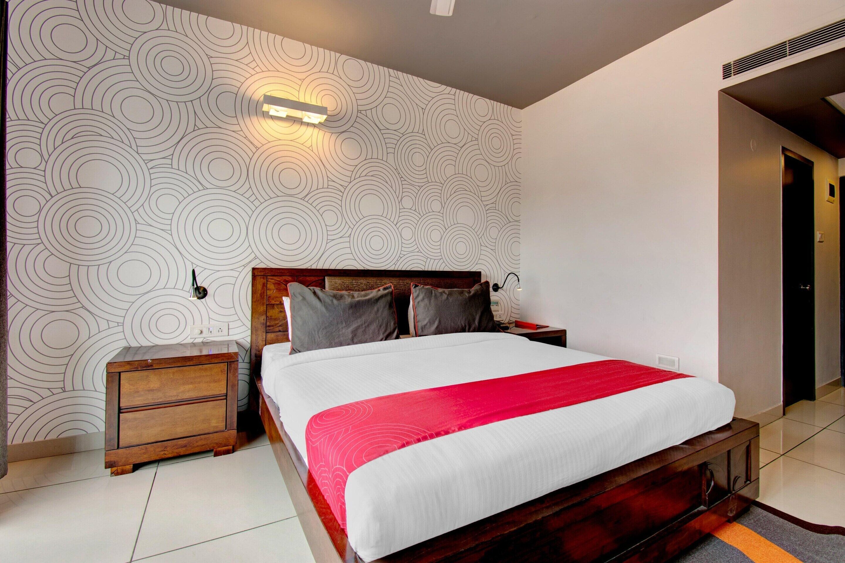 Una habitación de hotel moderna con una cama grande, una mesita de noche de madera y un papel tapiz estampado.