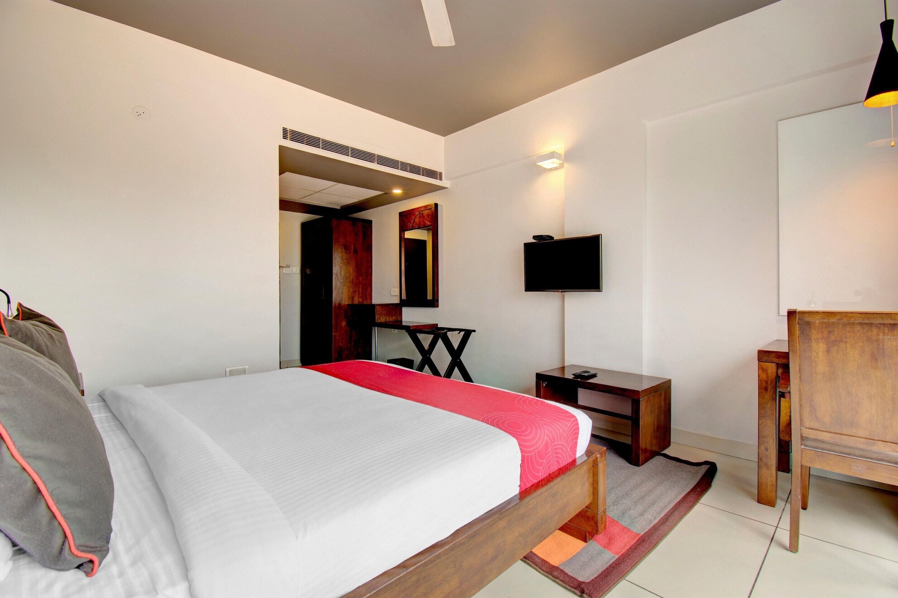 Una habitación de hotel con cama, escritorio, silla, televisión y espejo.