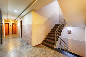 Rebedor d'hotel amb sòl de marbre, escala amb barana metàl·lica i un extintor a la paret.