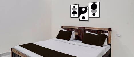 Een bed met een houten hoofdbord, wit beddengoed en twee zwarte kussens.