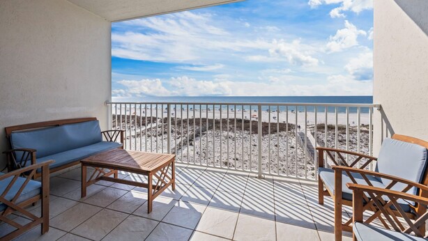 Ein Balkon mit Blick auf den Strand, einem Holztisch und zwei Holzstühlen.