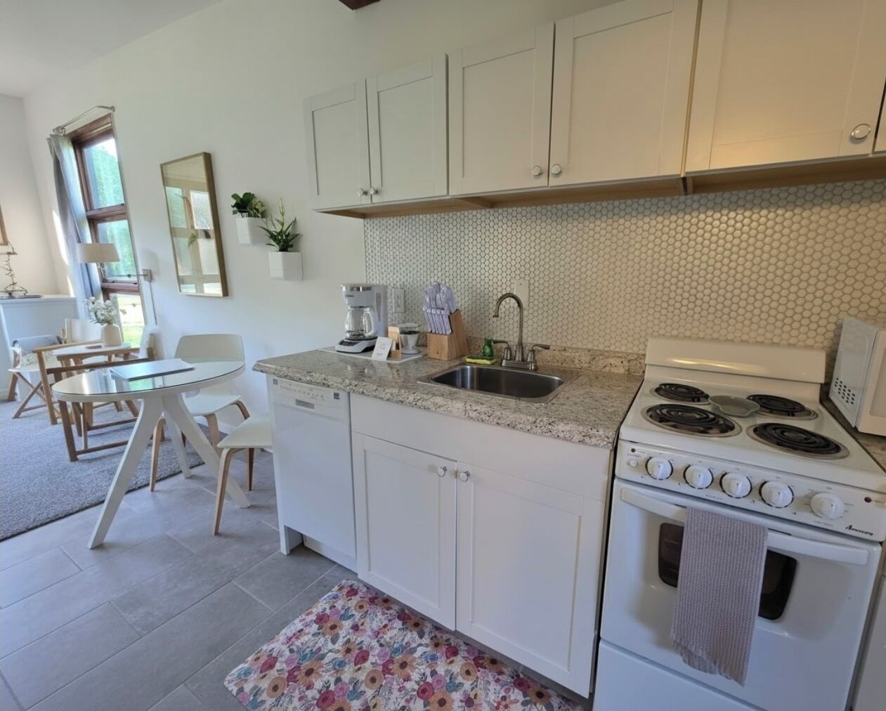 A kitchen with white cabinets, a gas stove, a sink, and a dining area with a table and chairs.