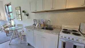 Een keuken met witte kasten, een gasfornuis, een spoelbak en een eethoek met een tafel en stoelen.