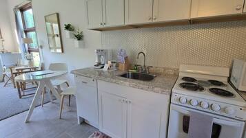 A kitchen with white cabinets, a gas stove, a sink, and a dining area with a table and chairs.