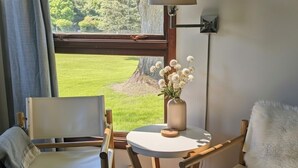 Een kamer met uitzicht op een groen gazon, een ronde tafel met een bloevas, en twee houten stoelen.