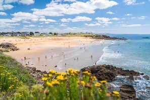 A beach with clear skies and calm waters, rocky coastline, and distant buildings. - Villa for 6 people with ocean view, pool, and hot tub, Le Pouldu (Clohars-Carnoët)