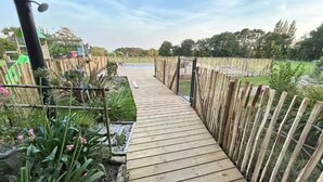 Un camino de madera que lleva a una zona de piscina, rodeada por una valla de bambú y diversas plantas.