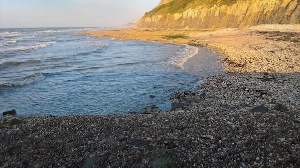 A rocky beach with waves, a cliff, and a clear sky.